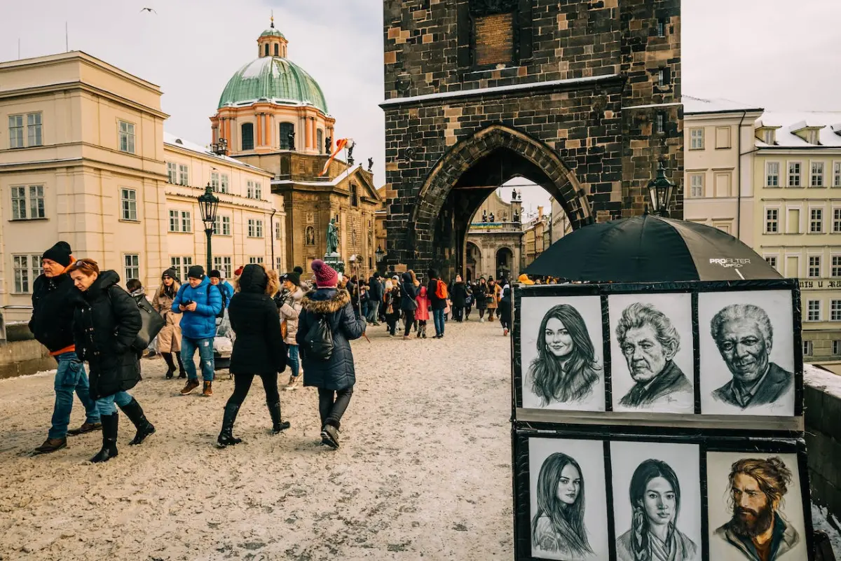 Tourists walk by painted faces on Charles Bridge in winter