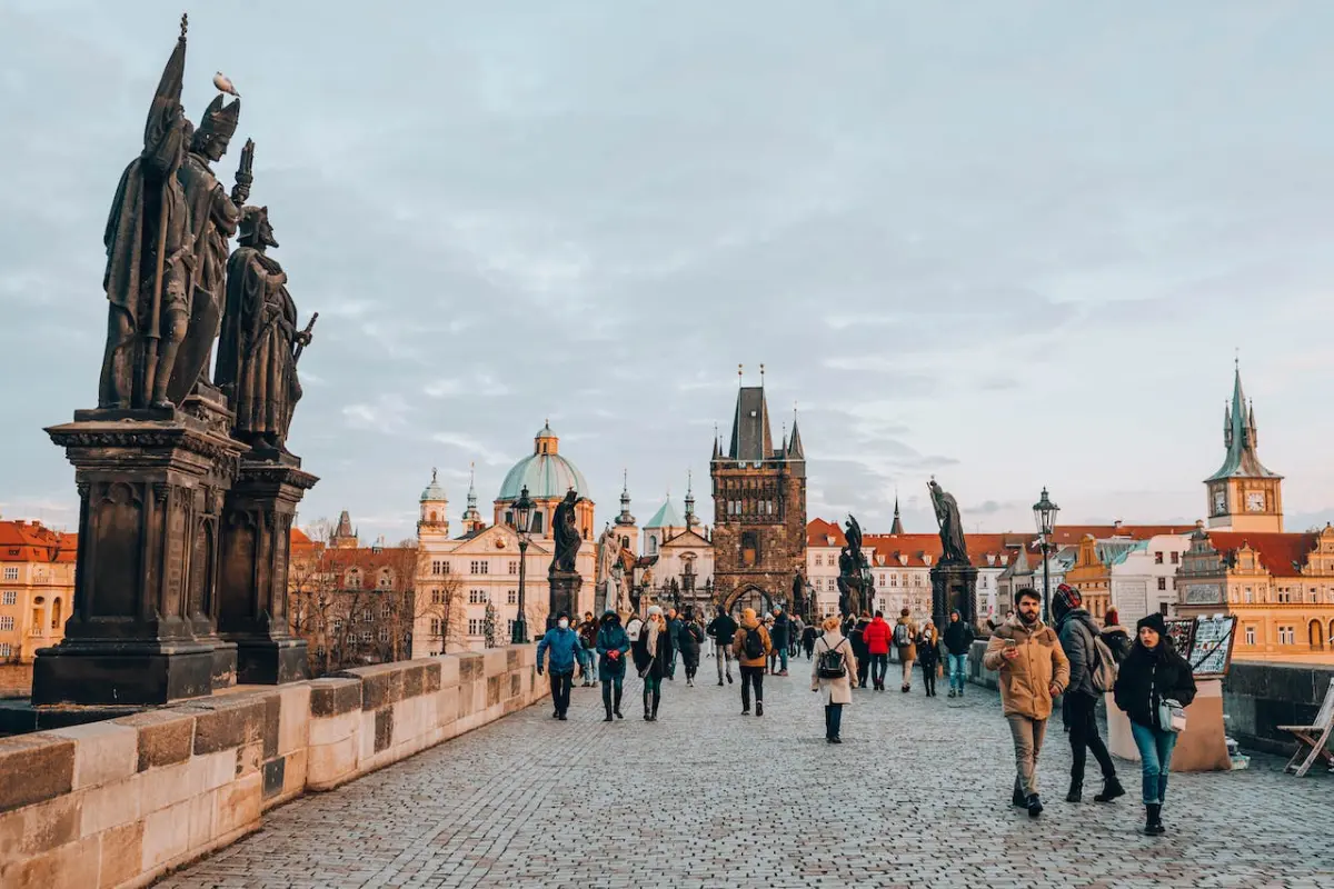 Daytime tourists stroll by statues on the Charles Bridge