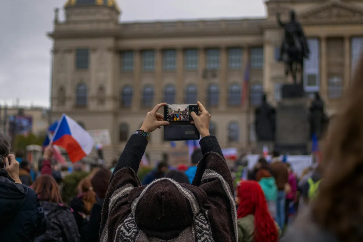 Tourist capturing the National Museum at Wenceslas Square amidst a crowd waving Czech Republic's flag