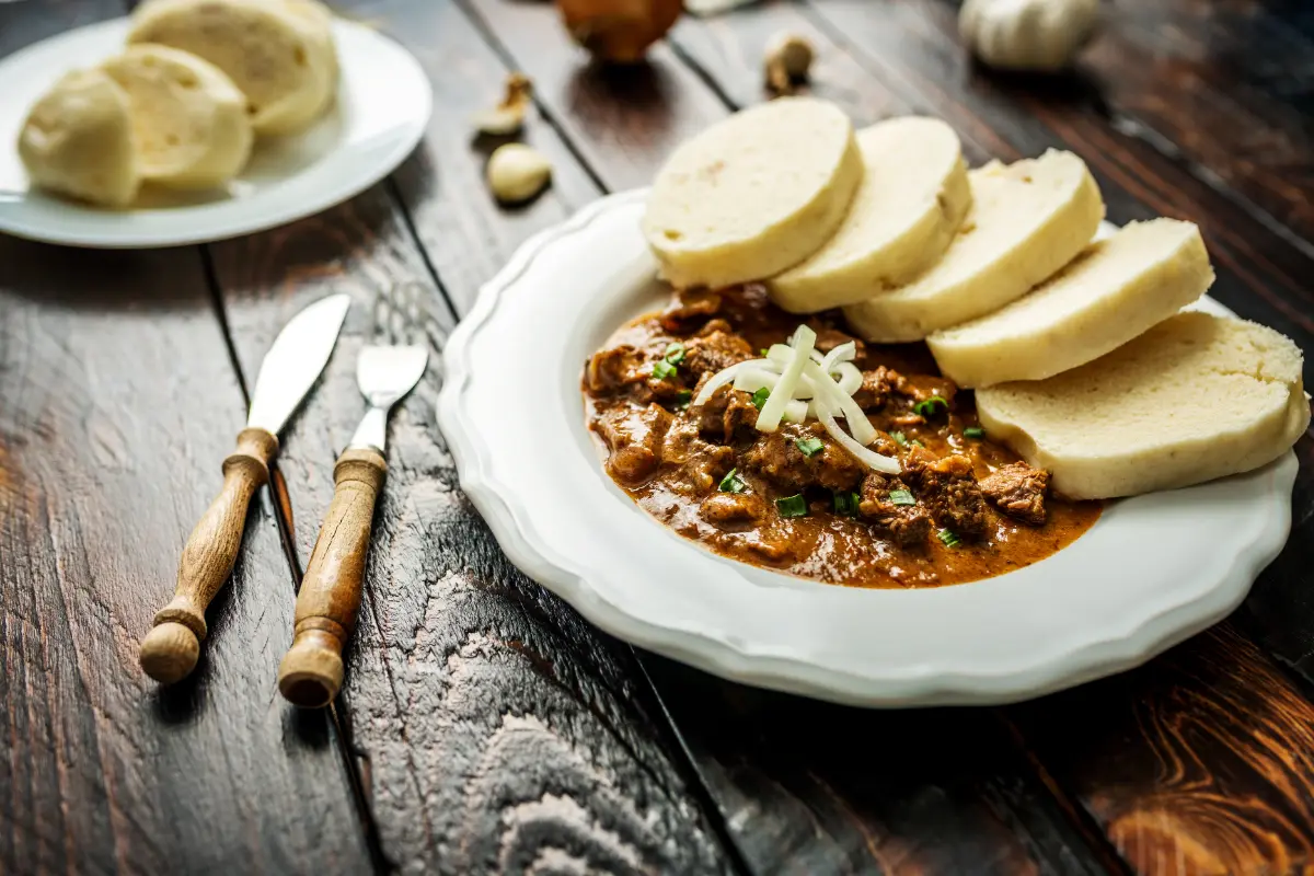 Traditional Czech goulash with dumplings and beer on wooden table